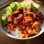 Close-up of crispy, glazed harissa chicken pieces served over white rice with fresh lettuce in a bowl.