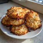 A stack of golden brown, toasted coconut almond joy cookies piled on a white plate.