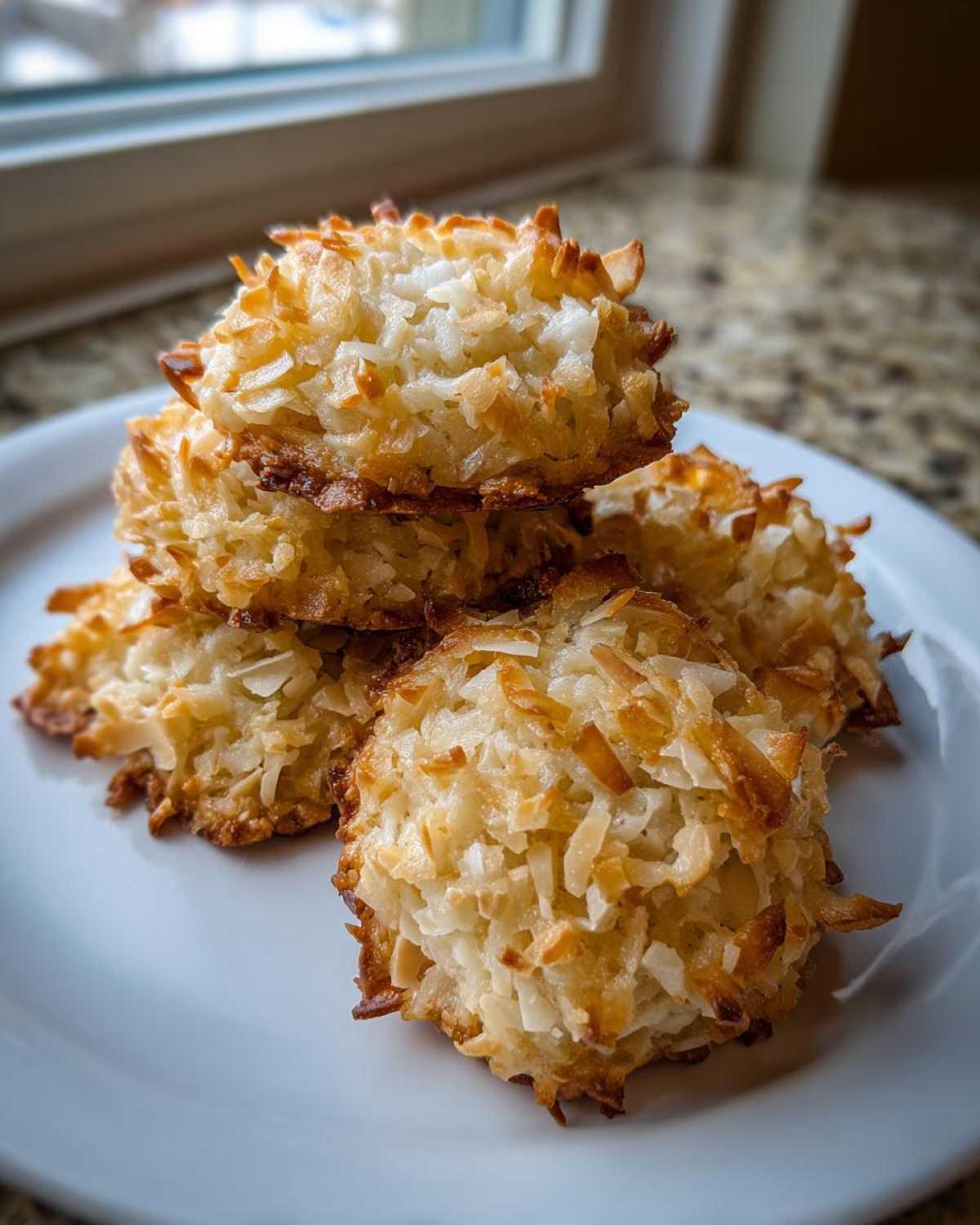 A stack of golden brown, toasted coconut almond joy cookies piled on a white plate.