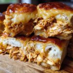 Close-up of gooey, cheesy bbq chicken sliders stacked on a wooden board, showing shredded chicken filling.