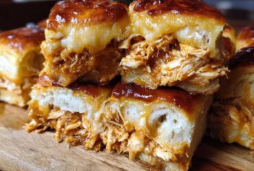 Close-up of gooey, cheesy bbq chicken sliders stacked on a wooden board, showing shredded chicken filling.