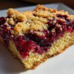 Close-up of a gooey slice of cherry dump cake showing the bright red cherry filling and crumb topping.