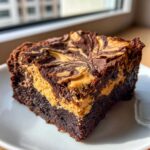 A close-up of a gooey peanut butter swirl brownies square served on a white plate.