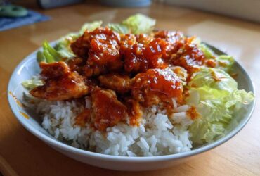 A bowl featuring saucy, glazed harissa chicken pieces served over white rice and surrounded by crisp lettuce.
