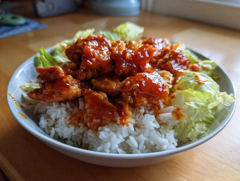 A bowl featuring saucy, glazed harissa chicken pieces served over white rice and surrounded by crisp lettuce.