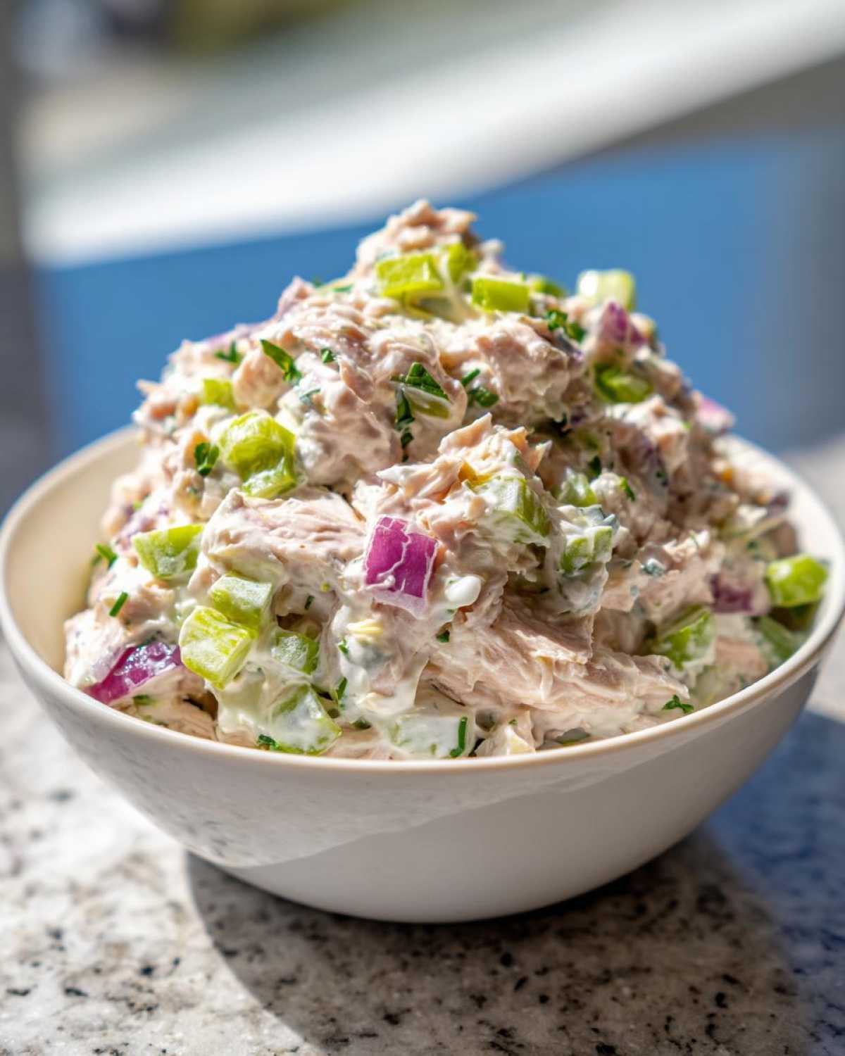 A white bowl filled high with creamy healthy tuna salad mixed with celery and red onion.