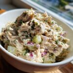 A close-up of a creamy, chunky healthy tuna salad mixed with red onion and celery in a white bowl.