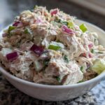 A close-up shot of creamy, chunky healthy tuna salad mixed with diced red onion and celery in a white bowl.