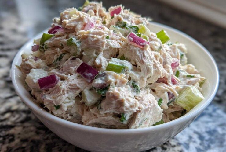 A close-up shot of creamy, chunky healthy tuna salad mixed with diced red onion and celery in a white bowl.