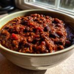 A close-up shot of a bowl filled with rich, thick black bean chili, illuminated by natural sunlight.