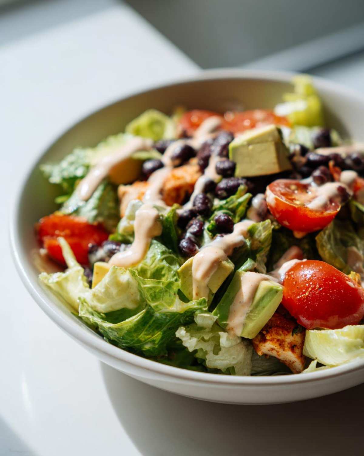 Close-up of a vibrant southwest salad featuring lettuce, black beans, avocado, tomatoes, and creamy dressing.