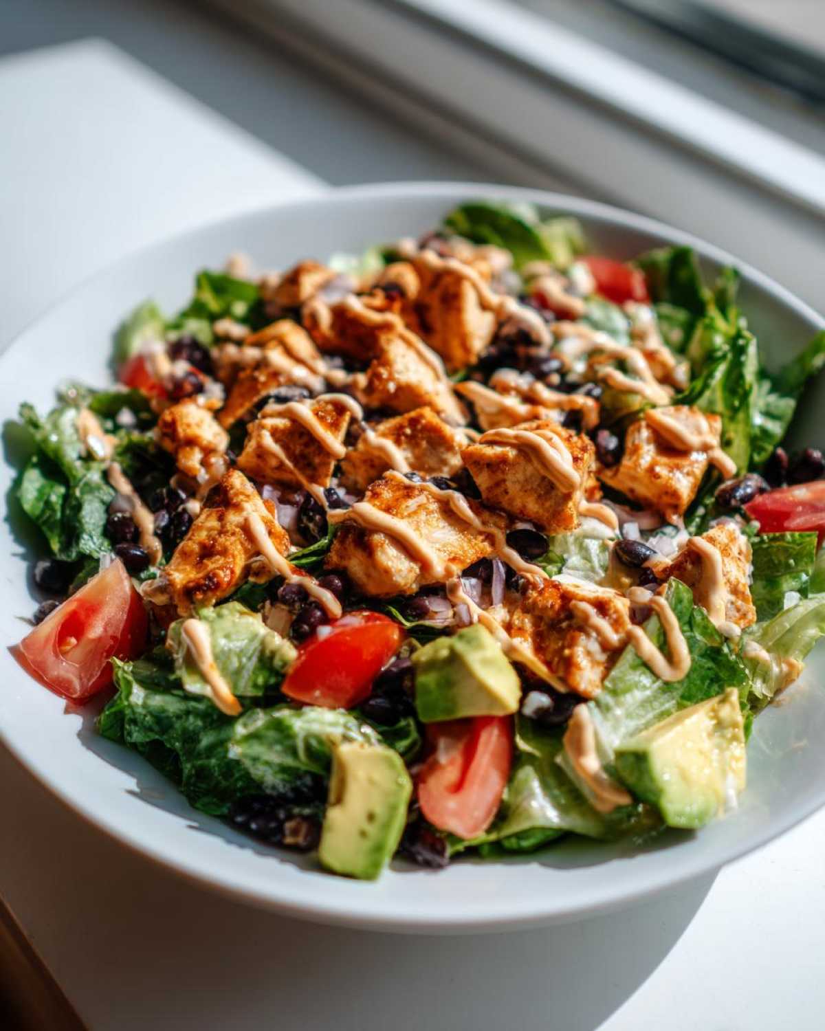 Close-up of a vibrant southwest salad featuring seasoned chicken, black beans, avocado, tomatoes, and a creamy drizzle.