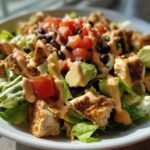 Close-up of a vibrant southwest salad featuring grilled chicken, avocado, black beans, tomatoes, and creamy dressing.