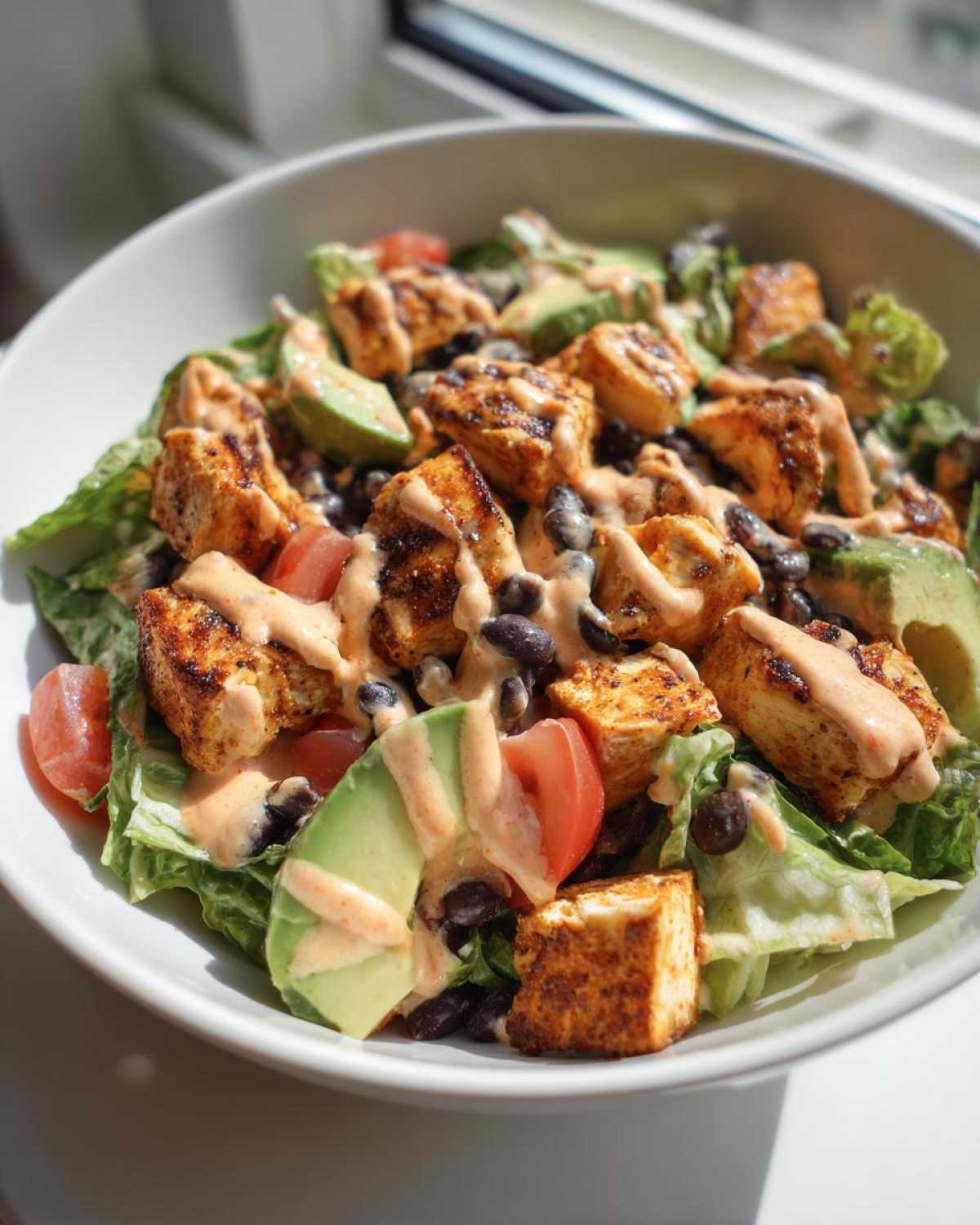 Close-up of a vibrant southwest salad bowl featuring seasoned tofu, black beans, avocado, tomatoes, and a creamy drizzle.