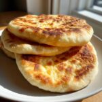 A stack of three golden-brown, freshly cooked homemade pita bread pockets resting on a light plate.