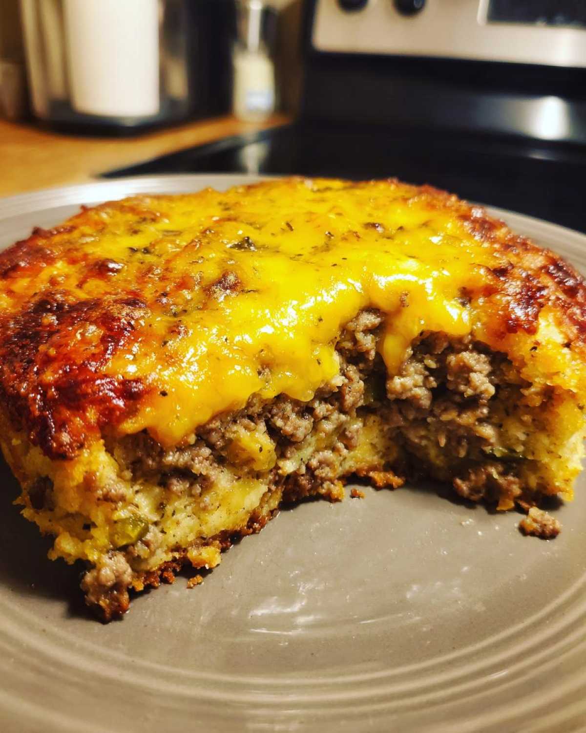 A close-up view of a portion of john wayne casserole showing the ground beef filling and melted cheddar cheese topping.