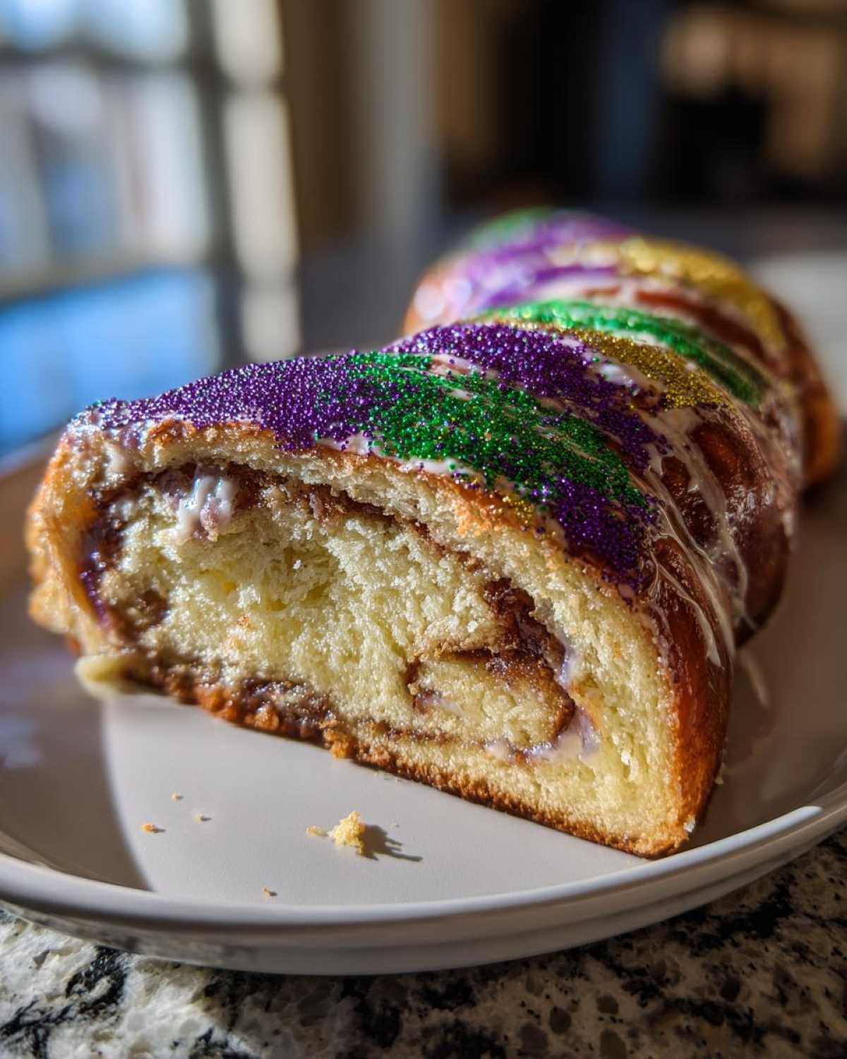 A slice of delicious king cake showing the swirl filling and colorful purple, green, and gold Mardi Gras sprinkles.