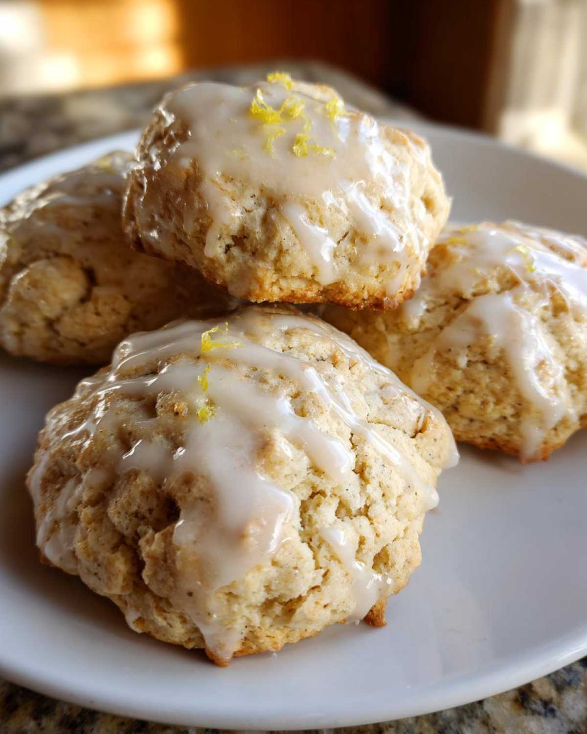 Close-up of four stacked, fluffy earl grey cookies topped with a white lemon glaze and bright yellow zest.