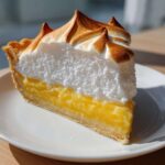 A tall slice of lemon meringue pie showing bright yellow curd and perfectly torched meringue peaks.