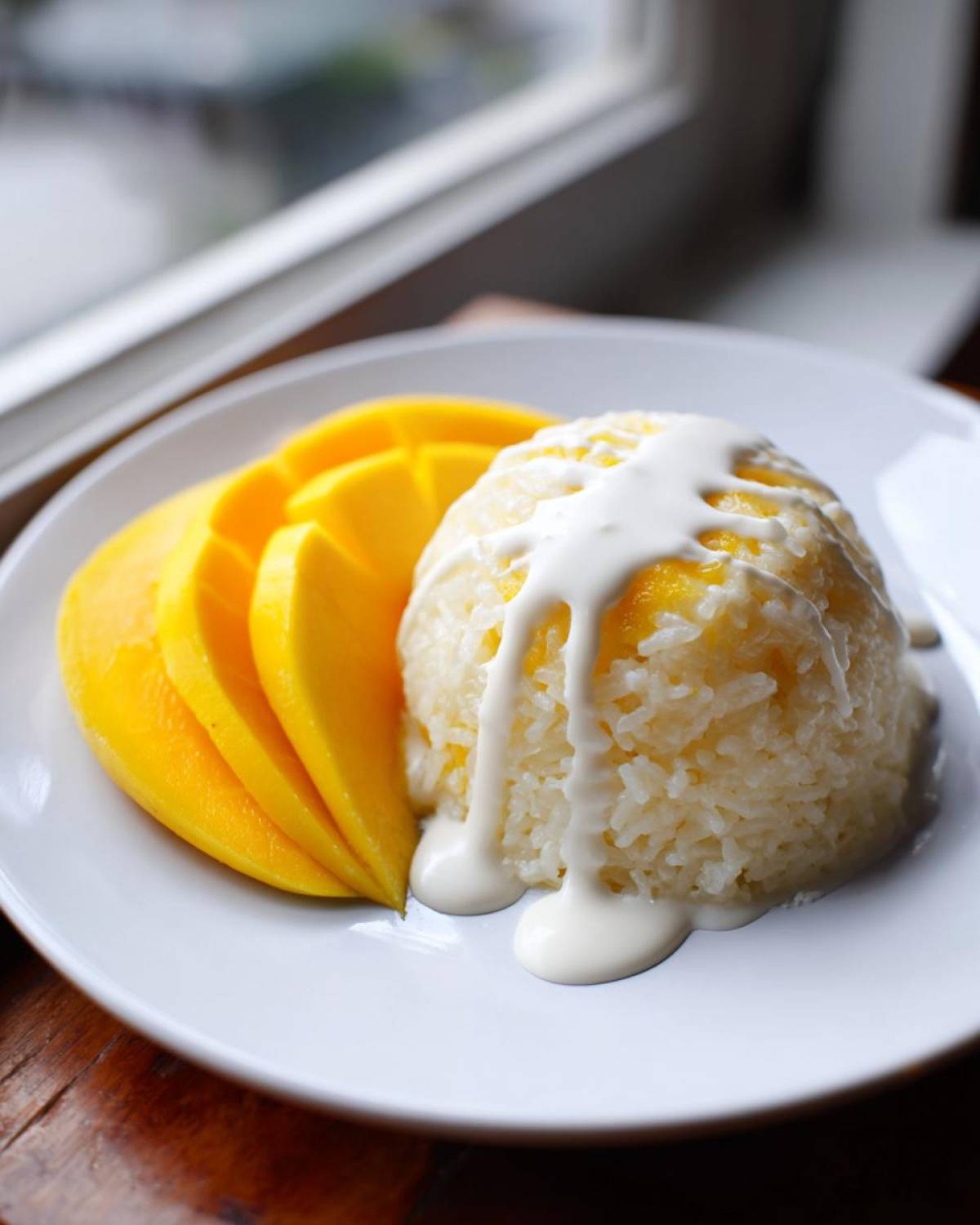 A serving of mango sticky rice, featuring sliced fresh mango next to a dome of sweet rice topped with creamy coconut sauce.