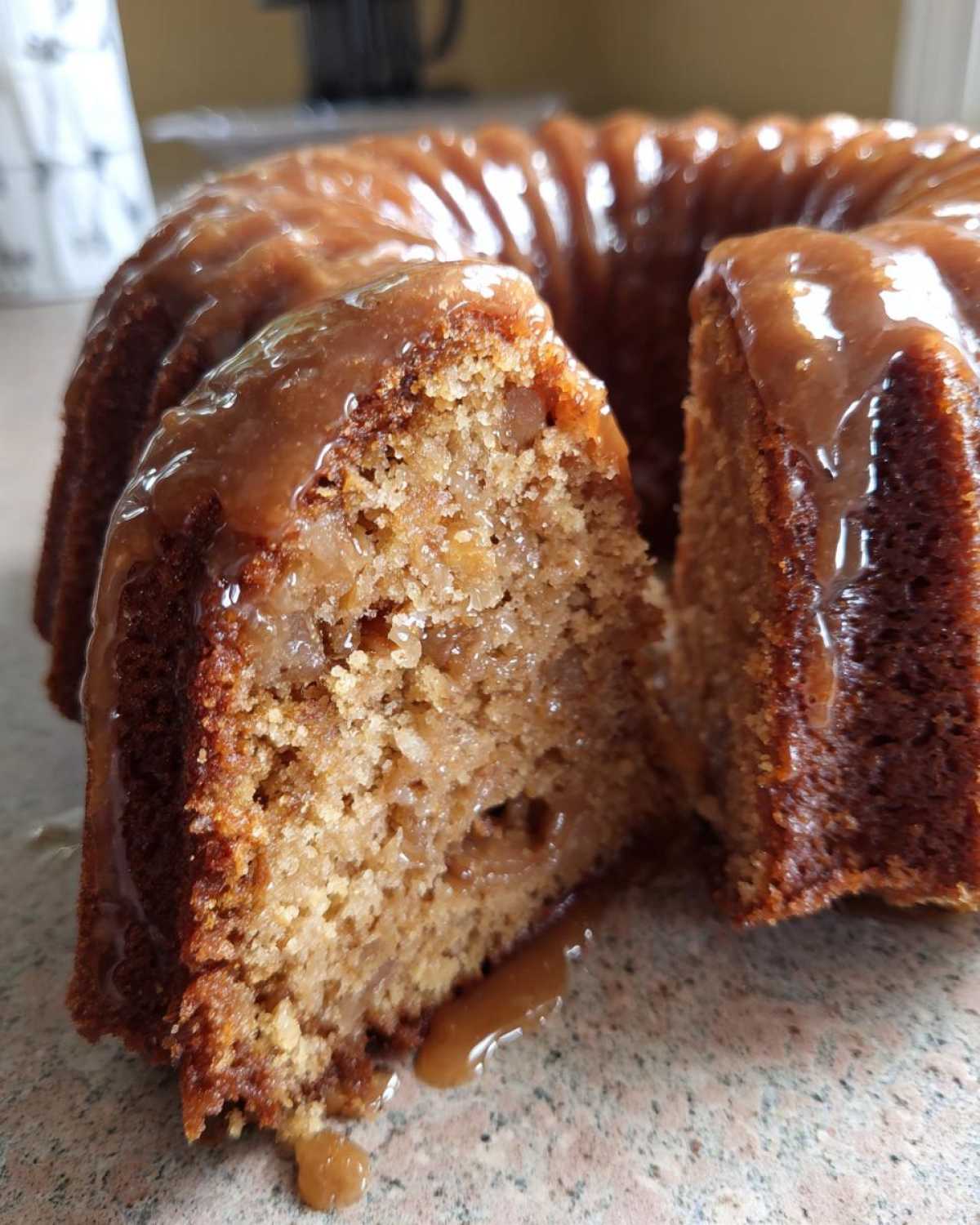 Close-up of a slice taken out of a moist apple bundt cake topped with a thick caramel glaze.