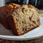 Close-up of a thick slice of moist banana bread recipe with visible chocolate chips on a white plate.