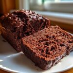 A rich, dark chocolate bread loaf, partially sliced, topped with chocolate chips.