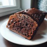 Close-up of a thick slice of rich, dark chocolate bread with visible chocolate chips on a white plate.