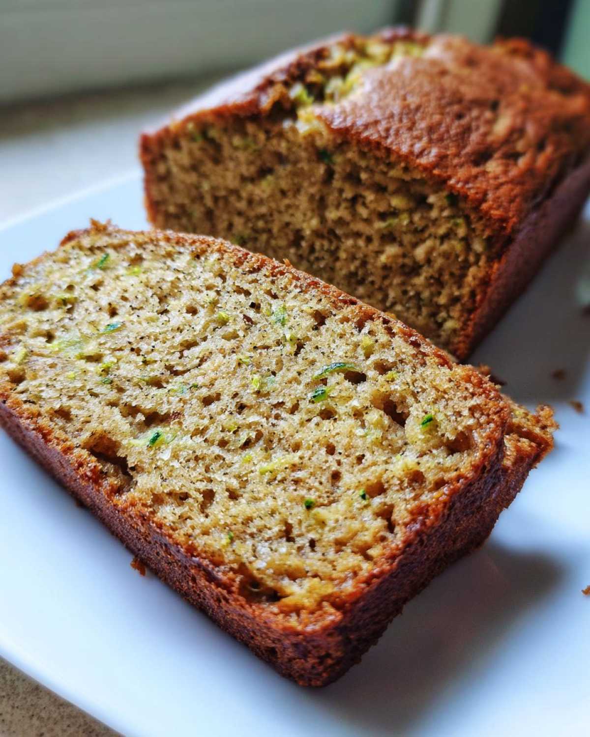 A close-up view of a moist slice of zucchini banana bread, showing the texture and flecks of green zucchini.