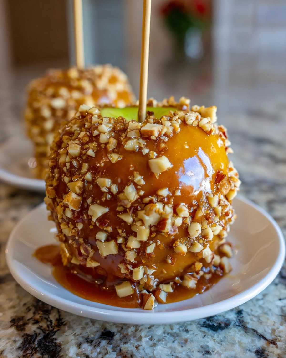 Close-up of a glossy caramel apple completely covered in chopped nuts, resting on a small white plate.