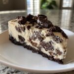 A thick slice of creamy Oreo cheesecake, packed with chocolate cookie pieces and topped with more crumbles.