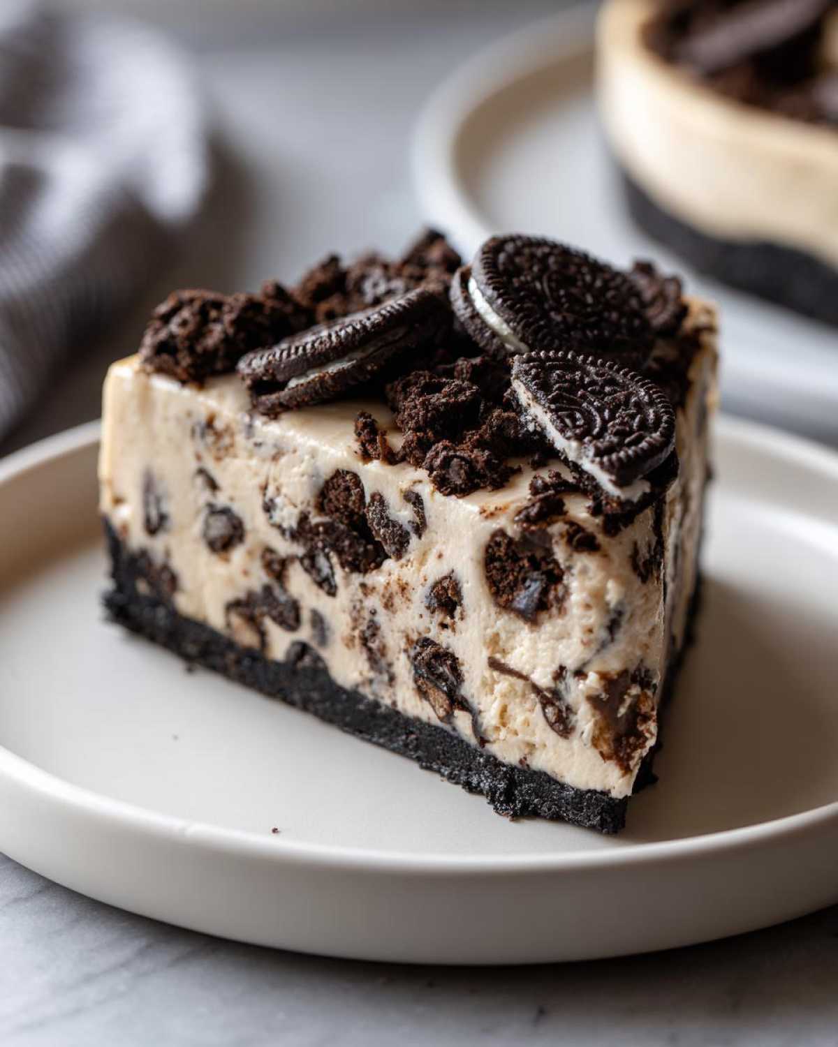 A decadent slice of Oreo cheesecake featuring a dark chocolate crust, creamy filling studded with cookie pieces, and topped with crushed Oreos.
