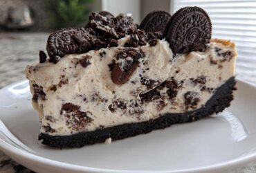 A thick slice of creamy Oreo cheesecake with a dark chocolate crust, topped with crushed and whole Oreo cookies.