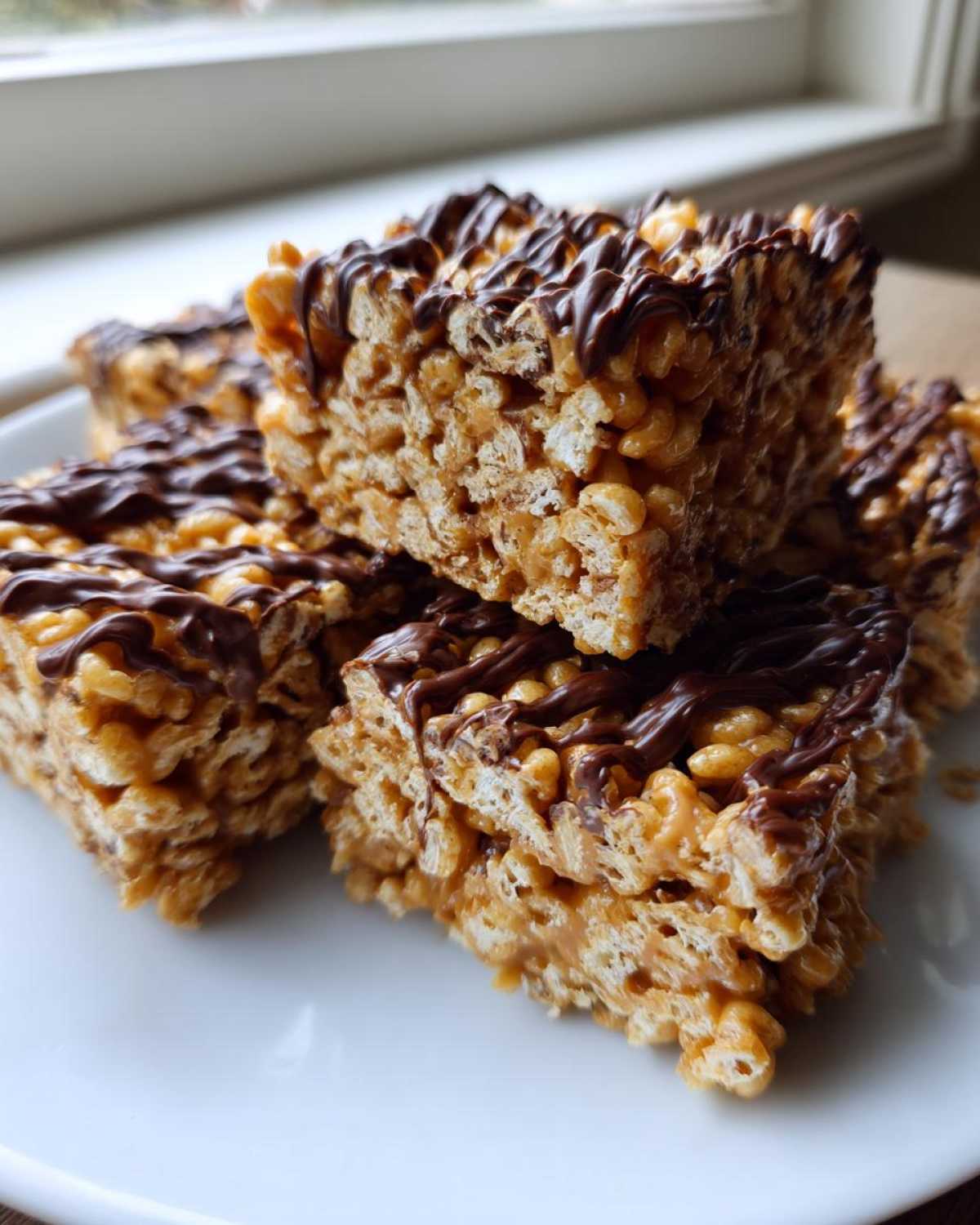 A stack of thick peanut butter rice krispie treats drizzled generously with melted dark chocolate.