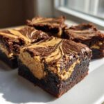 Close-up of four rich, fudgy peanut butter swirl brownies stacked on a white plate.