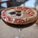 Close-up of a festive peppermint espresso martini garnished with crushed candy canes and three coffee beans.
