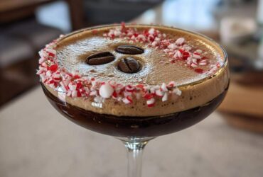 Close-up of a festive peppermint espresso martini garnished with crushed candy canes and three coffee beans.