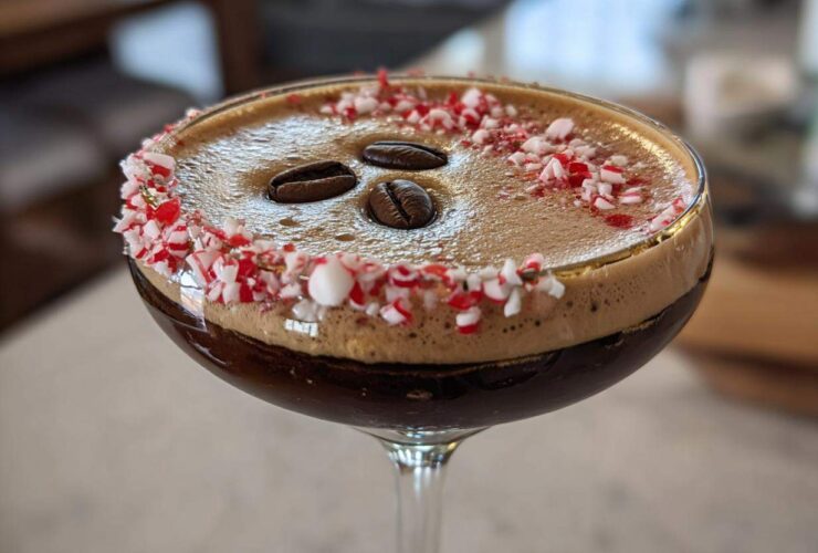 Close-up of a festive peppermint espresso martini garnished with crushed candy canes and three coffee beans.