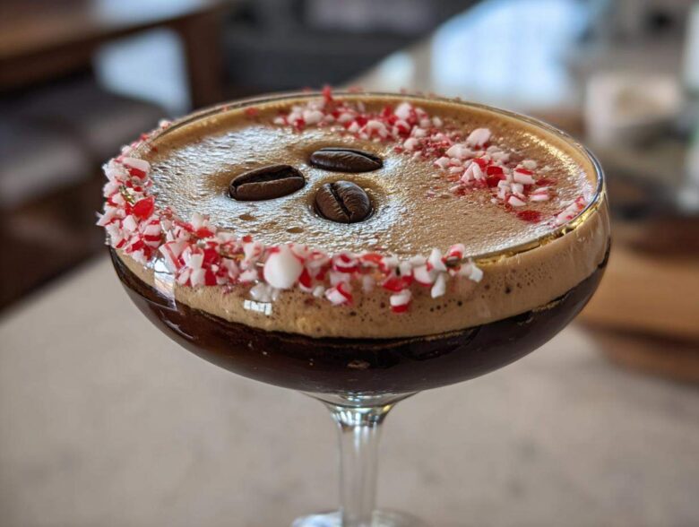 Close-up of a festive peppermint espresso martini garnished with crushed candy canes and three coffee beans.