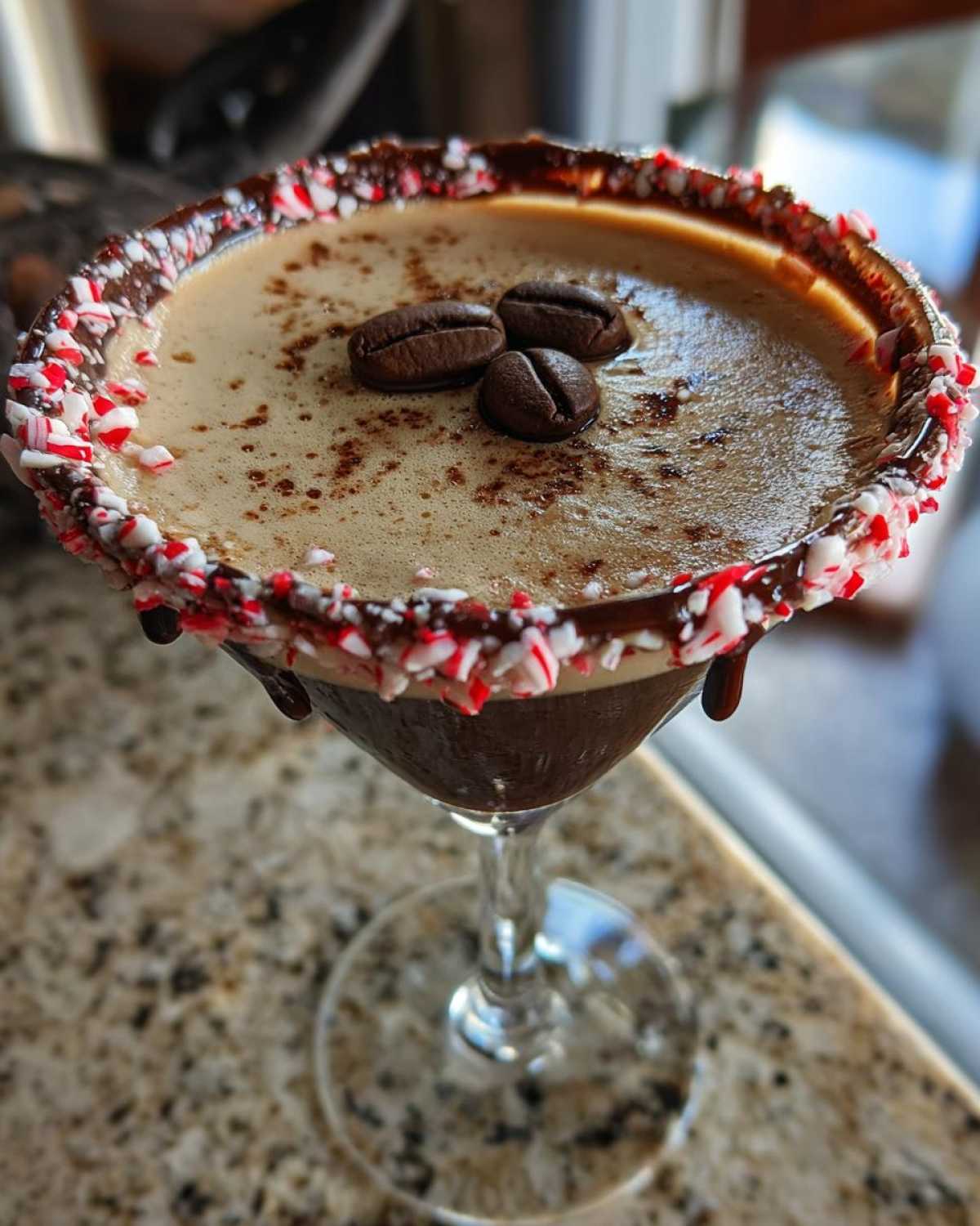 A festive peppermint espresso martini in a coupe glass with a chocolate and crushed candy cane rim, garnished with three coffee beans.