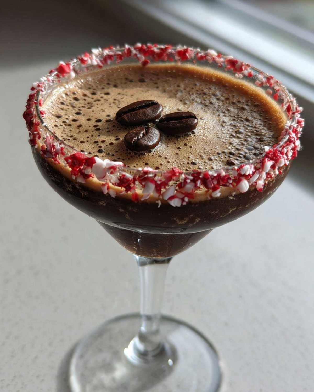 A festive peppermint espresso martini garnished with crushed candy canes and three coffee beans.
