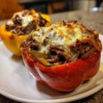 Close-up of two baked philly cheesesteak stuffed peppers, topped with melted, browned cheese.