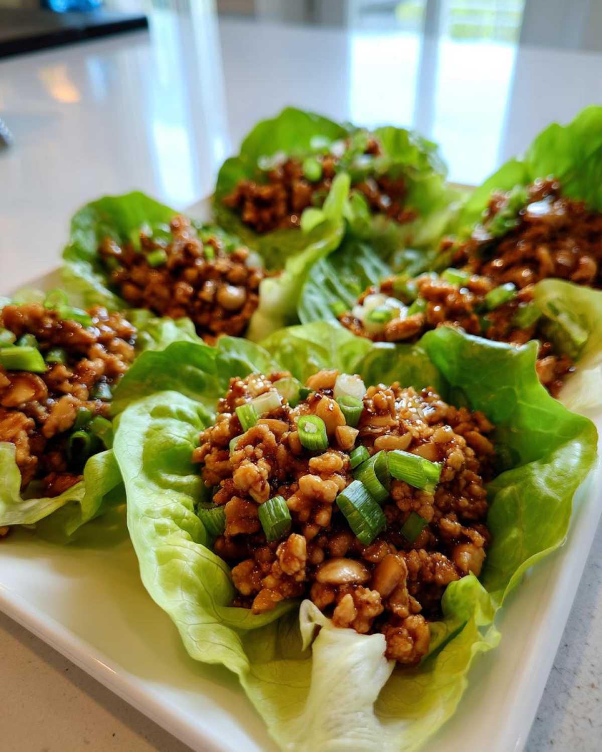 Close-up of several fresh chicken lettuce wraps filled with savory ground chicken mixture and topped with chopped green onions.