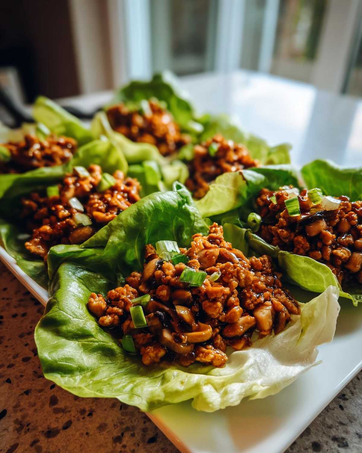 Several servings of delicious chicken lettuce wraps filled with savory ground chicken and mushrooms, garnished with green onions.