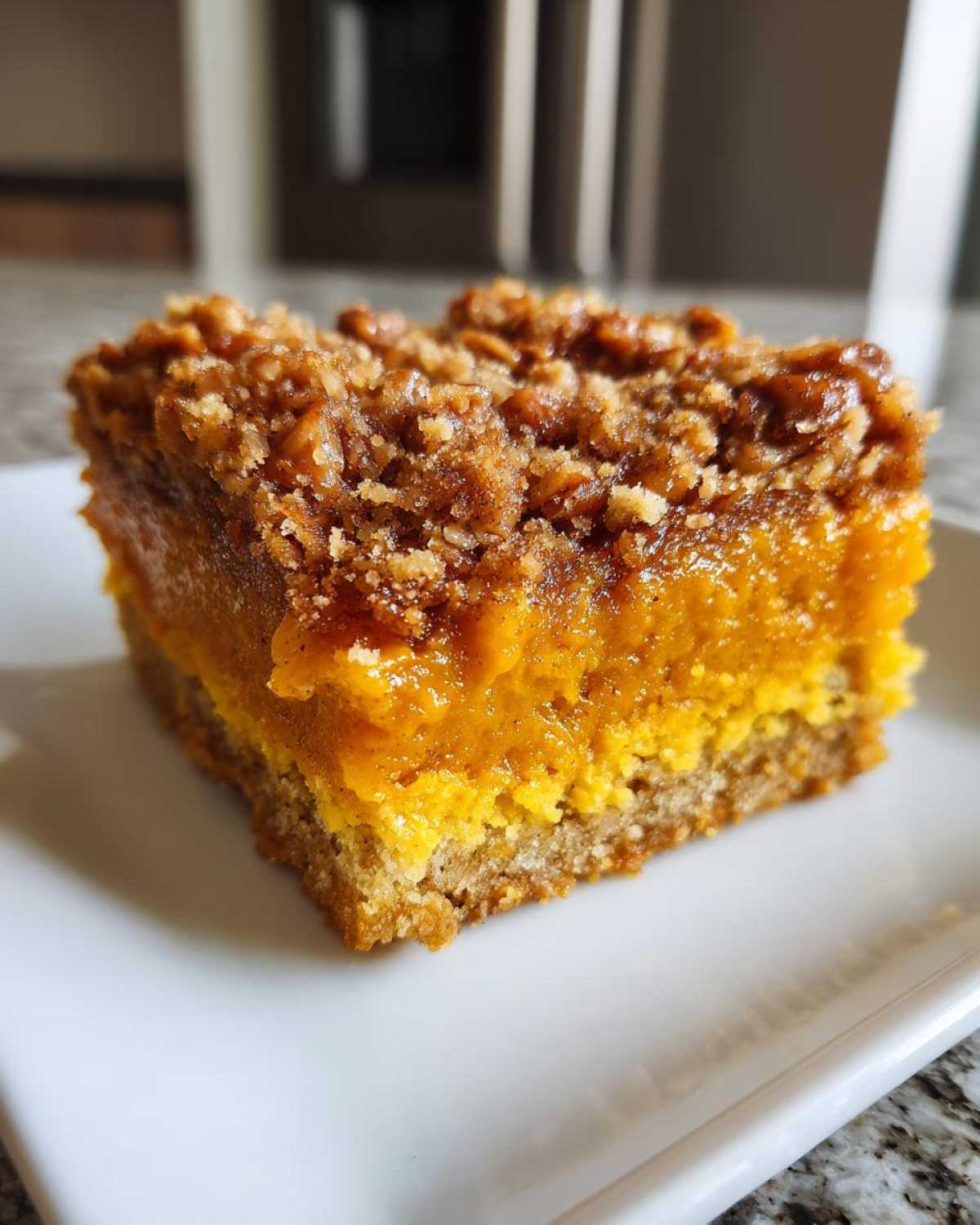 Close-up of a square slice of pumpkin crunch dessert showing a cake base, bright orange pumpkin layer, and crumbly topping.