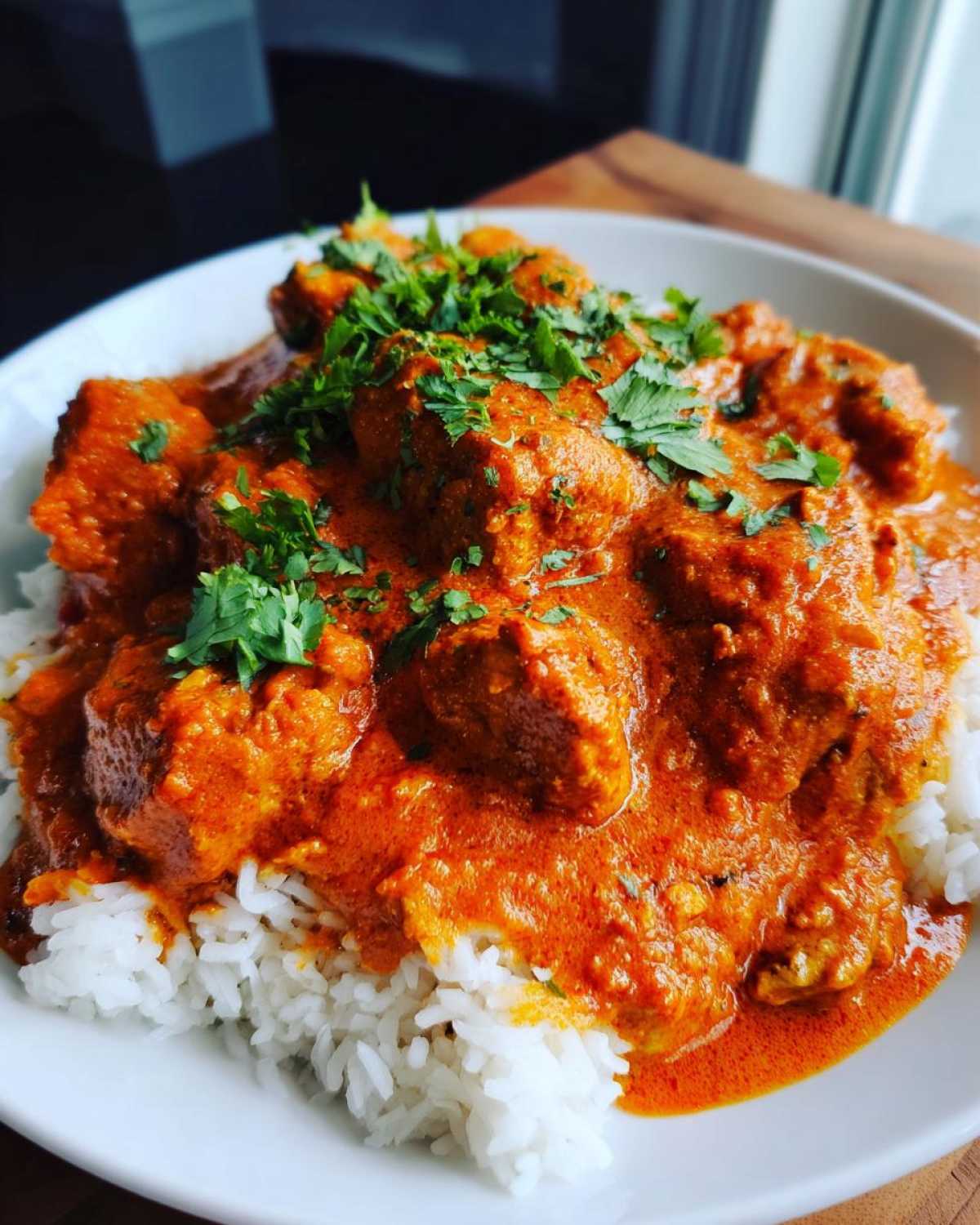 A close-up of creamy, orange butter chicken served over a bed of fluffy white rice and garnished with fresh cilantro.