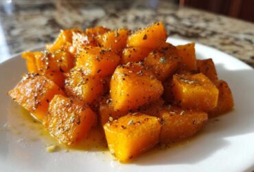 A close-up of bright orange roasted butternut squash cubes seasoned with herbs on a white plate.