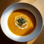 A vibrant bowl of roasted butternut squash soup, garnished with a cream swirl and fresh thyme.
