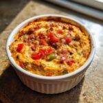 Close-up of hot sausage cream cheese dip baked golden brown with diced red and green peppers in a white ramekin.