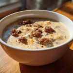 Close-up of a white bowl filled with creamy sausage potato soup, topped with browned sausage crumbles.